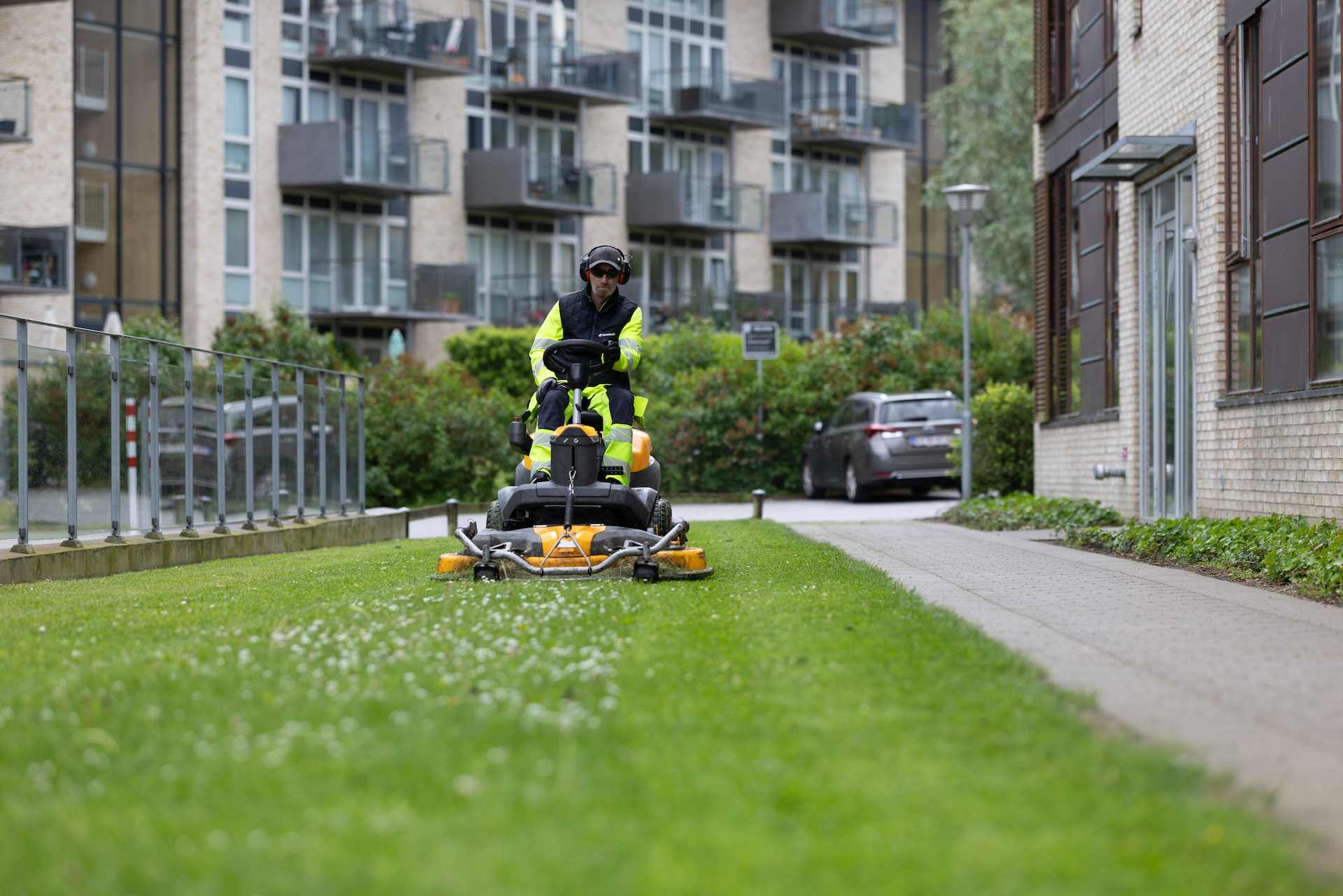 Ejendomsservicemedarbejder slår græs mellem boligblokke